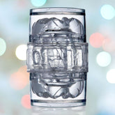 The Fleshlight Quickshot Vantage Open-Ended Masturbating Sleeve, a transparent cylindrical device made of Superskin and featuring intricate internal textures, is presented against a blurred background of colorful lights.